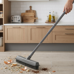 Person using a broom to clean a kitchen floor with wooden cabinets and a toaster in the background.