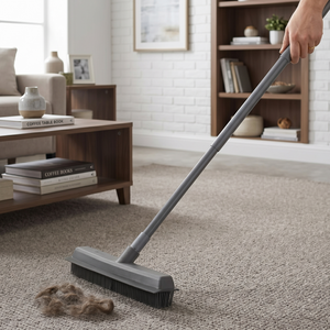 Person using a broom to collect hair on a carpet in a living room.